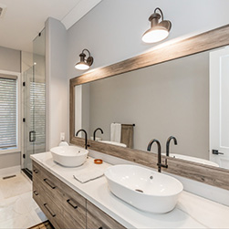 A bathroom white counter renovation with two white rounded sinks, black faucets and a mirror