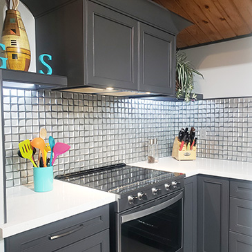 Kitchen renovation with white countertops, black cabinets and stove, with glass tiling backsplash