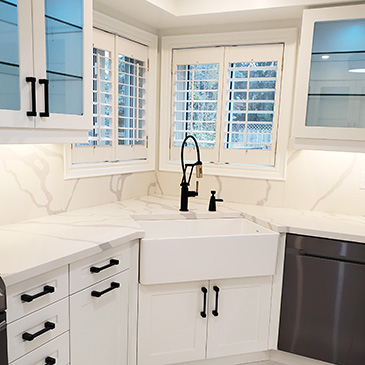 Kitchen renovation with white granite countertop and backsplash with white cabinets and a white rectangular sink
