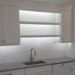 Kitchen renovation with white tile backsplash, white cabinets, a grey granite countertop and stainless steel sink